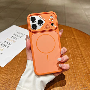 An orange magnetic phone case with a built-in stand, held by a hand over a wooden table. The case features a large circular MagSafe-compatible magnetic ring on the back, a raised camera bumper, and a small speaker grille.